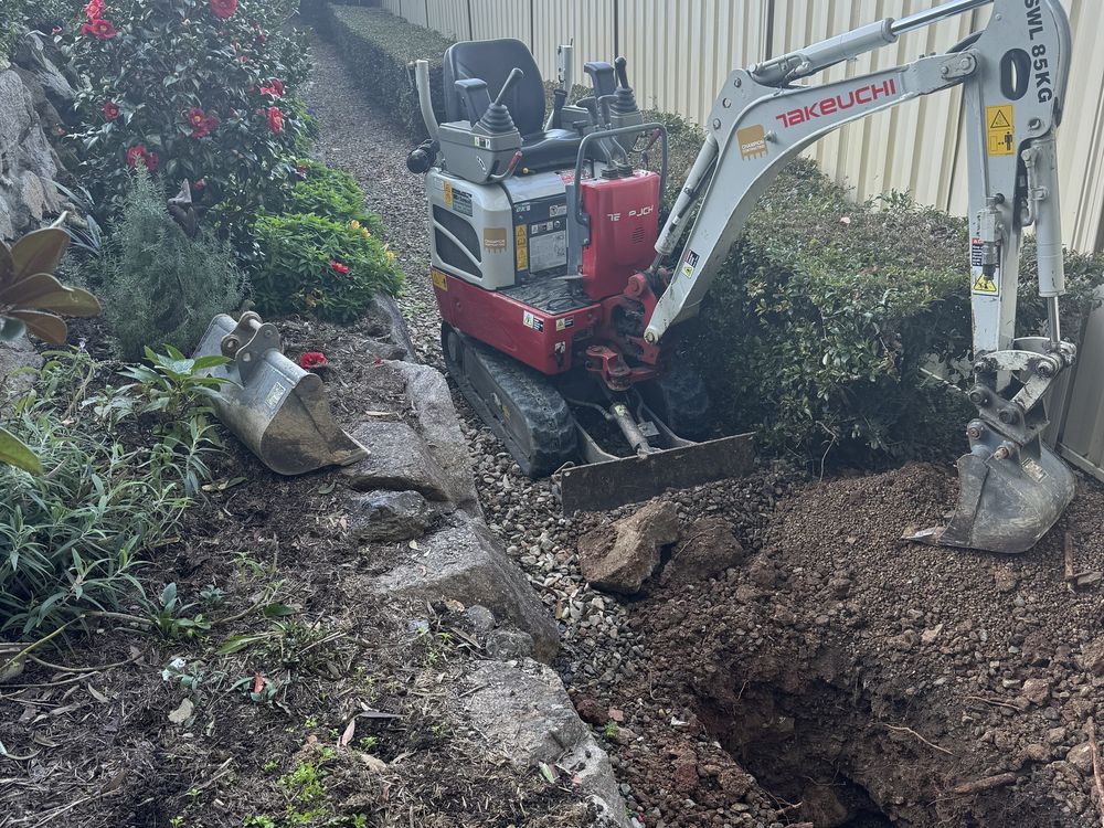Mini excavator digging a trench down the tight side access of a Brisbane home
