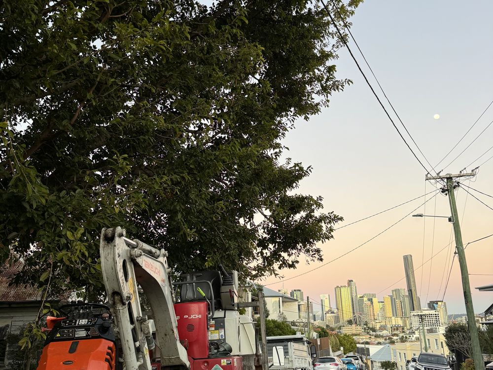 Mini excavator on a Brisbane street with the city skyline behind