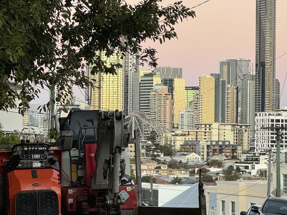 Compact excavator loaded up on site with the Brisbane city skyline behind
