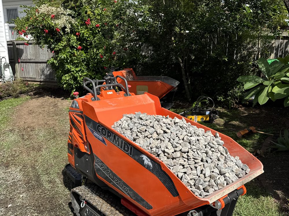 Tracked mini dumper carrying gravel through a backyard