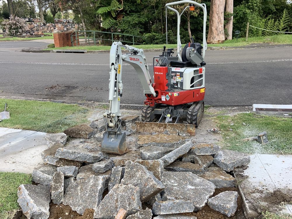 Mini excavator breaking up a concrete driveway for removal