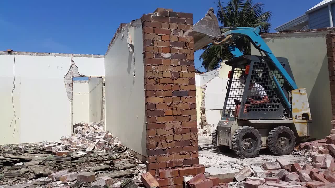 Compact machine demolishing a brick wall in a tight access yard