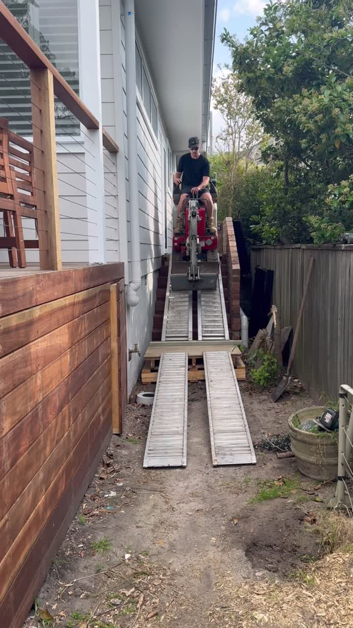 Mini excavator driving up ramps through a narrow side access
